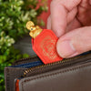 A hand is holding a small, orange-red leather pouch with a gold tortoise figurine on top.