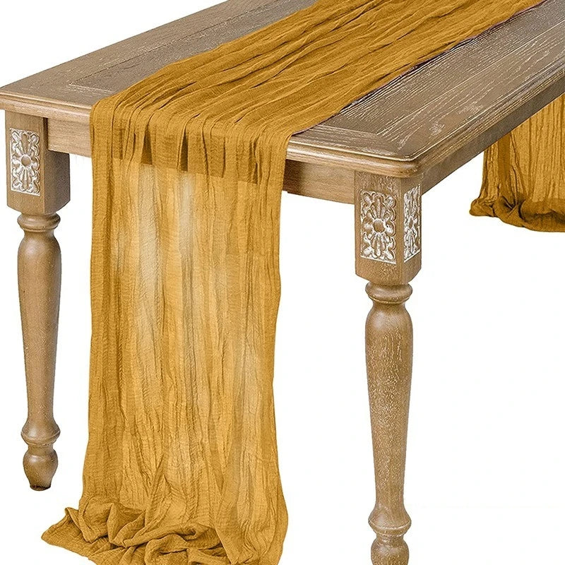 A flowing, semi-sheer gauze table runner in sage green draped over a wooden table.