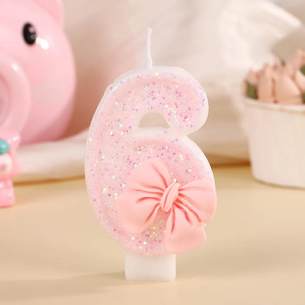 A pink glitter birthday candle shaped like the number 6 with a bow, set against a soft background.