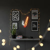 Décor mural LED néon avec art encadré et forme de cigarette lumineuse sur un mur gris foncé.