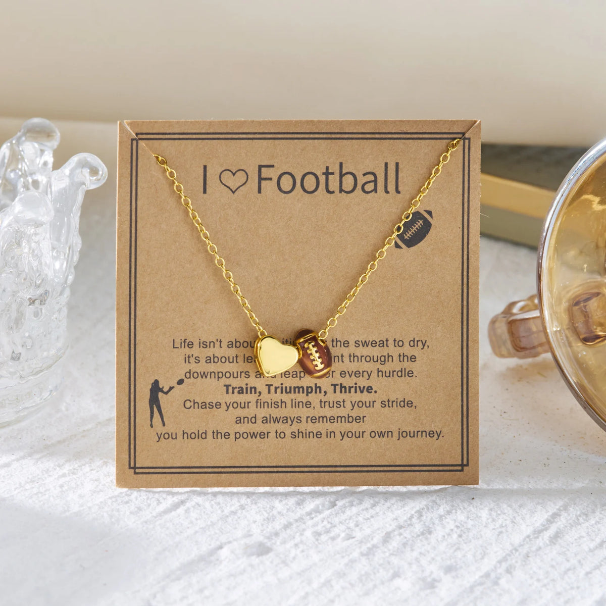 A gold chain necklace with a heart basketball pendant is displayed on a kraft paper card.