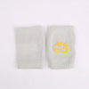 A pair of light gray knitted knee pads for infants featuring a yellow dinosaur design.