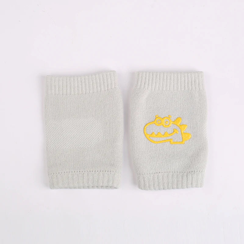 A pair of light gray knitted knee pads for infants featuring a yellow dinosaur design.