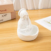 A white resin statue of the Virgin Mary with a veil sitting in a bowl on a wooden table.