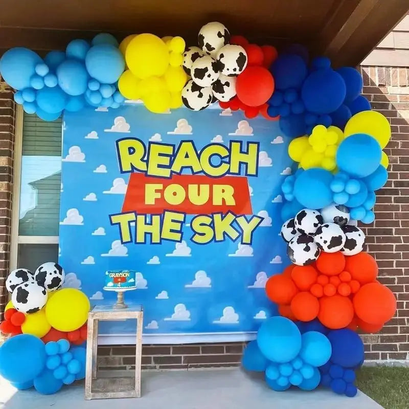 A colorful balloon arch featuring blue, yellow, and red latex balloons with cloud and cow print patterns for party decor.