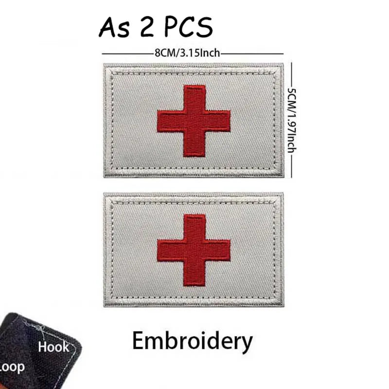 Two gray embroidered medical cross patches with silver edges and a black hook loop.