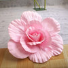 A large, pink silk foam rose flower with layered petals is displayed on a wooden surface.