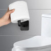 A hand is placing a white cloth or towel onto an adhesive cap holder hook mounted on a gray wall above a white toilet.