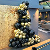 A large arrangement of black and gold confetti balloons displayed against a textured wall.