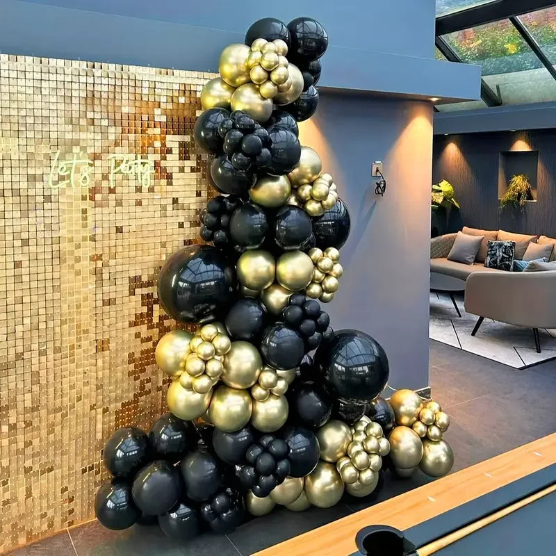 A large arrangement of black and gold confetti balloons displayed against a textured wall.