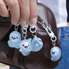 A hand holds several glow-in-the-dark ghost keychains attached to a brown leather bag.