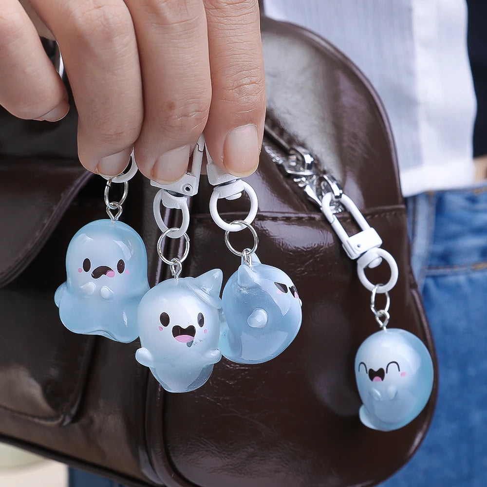 A hand holds several glow-in-the-dark ghost keychains attached to a brown leather bag.