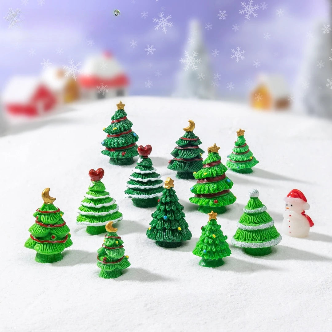 A collection of miniature green Christmas tree resin charms scattered on a white snowy surface with snowflakes in the backgro