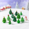 A collection of miniature green Christmas tree resin charms scattered on a white snowy surface with snowflakes in the backgro