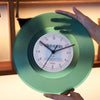 A hand holds a vintage vinyl record wall clock with a green transparent cover displaying the midnight time.