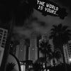 Black and white night photo of a palm tree silhouetted against a city skyline with a sign reading The World Is Yours