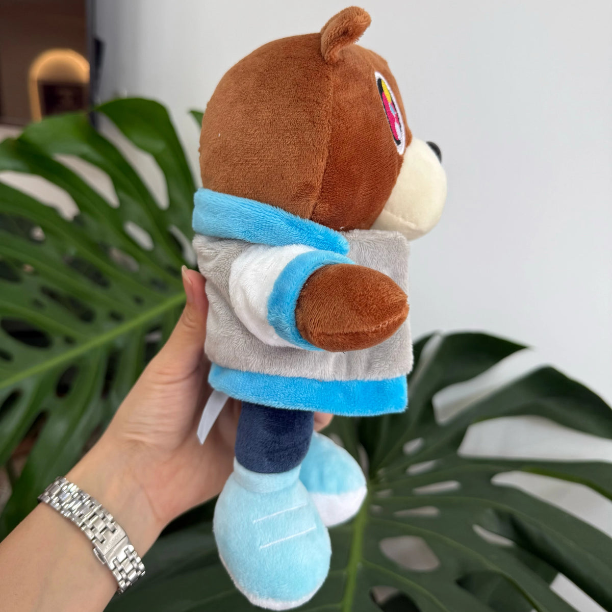 A hand holds a graduation bear plush toy wearing a blue and gray graduation stole.