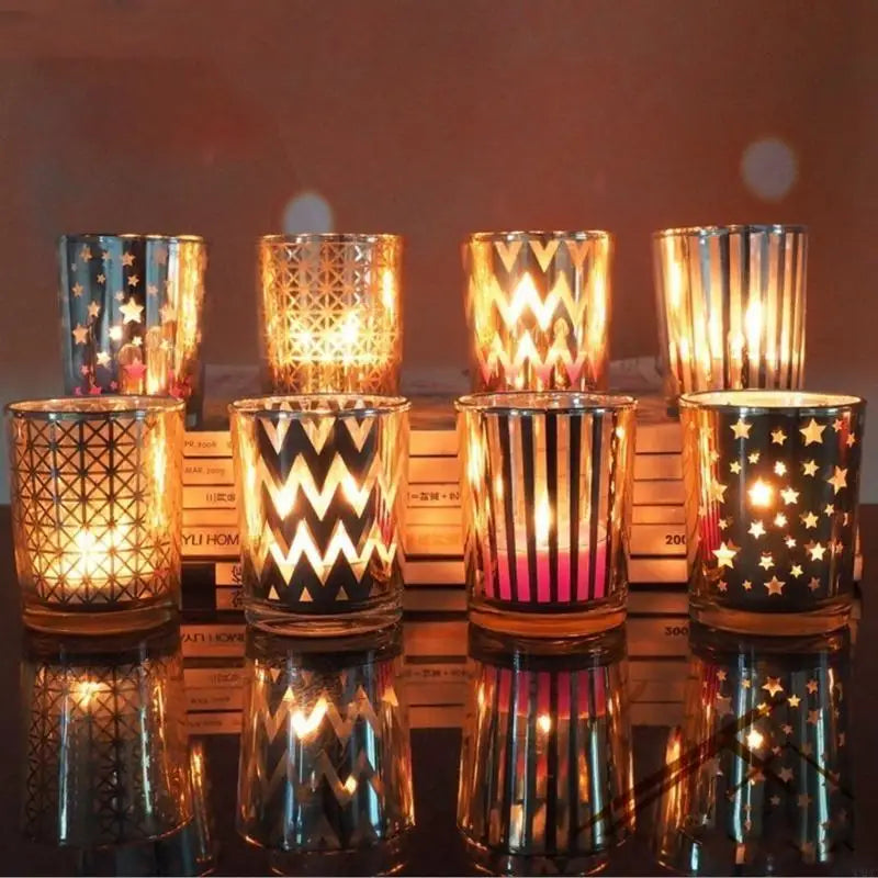A row of eight elegant glass votive candle holders with patterned designs and warm light, displayed on a reflective surface.