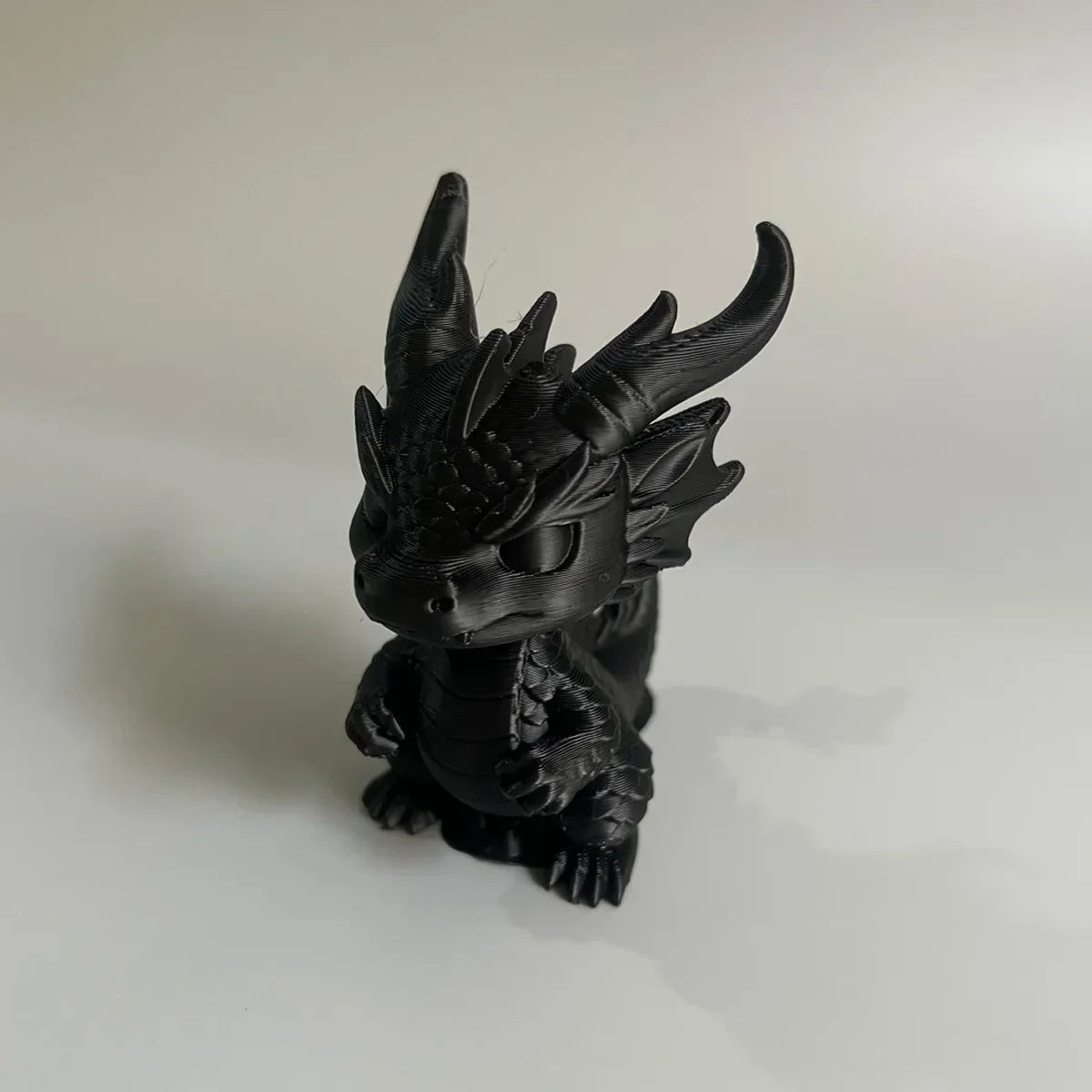 A black 3D printed mini dragon statue collectible with horns and detailed texture.