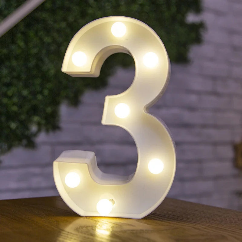 A glowing warm white LED alphabet letter light shaped like the number three resting on a wooden surface.