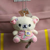 A fluffy white Rilakkuma plush bear with pink accents is attached to a keychain and displayed against a pink bag.
