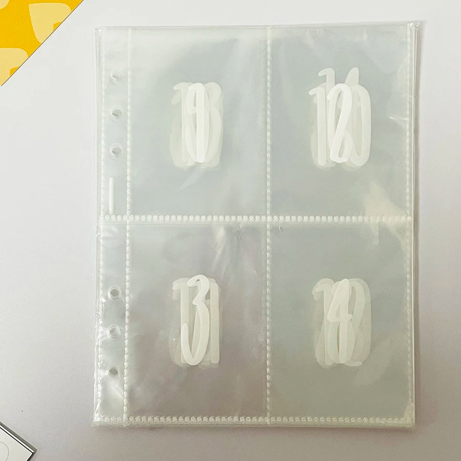 A clear plastic binder with numbered pockets for a savings challenge, showing numbers 10, 12, 13, and 14.