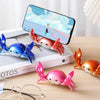 A pink crab-shaped desk organizer holding a pen and a smartphone on a wooden surface.