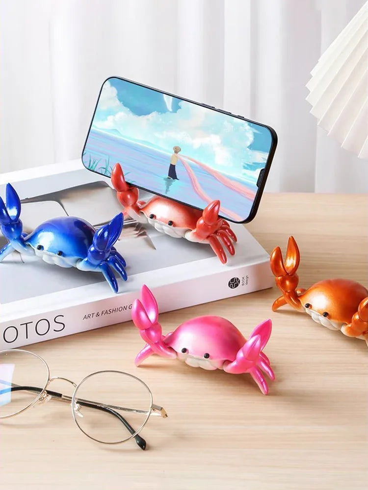 A pink crab-shaped desk organizer holding a pen and a smartphone on a wooden surface.