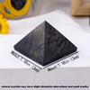 Pirámide de cristal de shungita gris oscuro sobre una superficie blanca con marcas de dimensión.