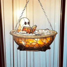 A glass hanging decoration featuring a ghost figure reading an open book submerged in glowing amber liquid.