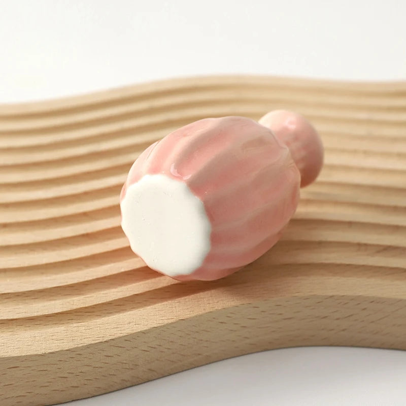 A pink ceramic mini vase resting on a light wooden surface.