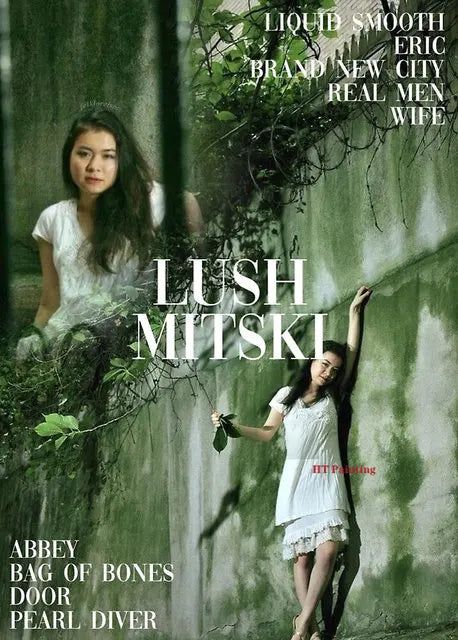 A portrait of Mitski in a white dress leaning against a green wall with foliage, featuring text for the album Lush.