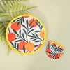 A round, yellow-rimmed fabric item featuring a pattern of orange and green leaves and fruit, used as a portable cooling fan.