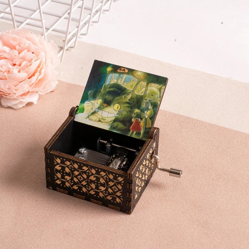 A hand-cranked wooden music box featuring a Totoro design, resting on a beige surface.