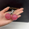 A hand holds a pink glittery cherry charm bag pendant with a silver keychain on a black background.