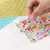 A hand is placing colorful self-adhesive rhinestones onto a white surface.