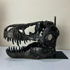 A dark resin sculpture of a realistic dinosaur skull with prominent teeth and eye sockets.