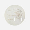 A light wood disc featuring a line drawing of a hand holding a finger, with the text me voilà.
