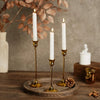 A set of three vintage European style metal candle holders with white candles resting on a wooden surface.