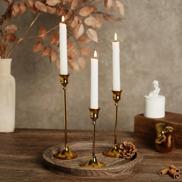 A set of three vintage European style metal candle holders with white candles resting on a wooden surface.