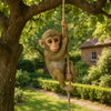 A small monkey figurine made of resin is hanging from a tree branch in a garden setting.