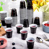A collection of black and white striped mini plastic shot cups filled with red liquid on a white marble surface.
