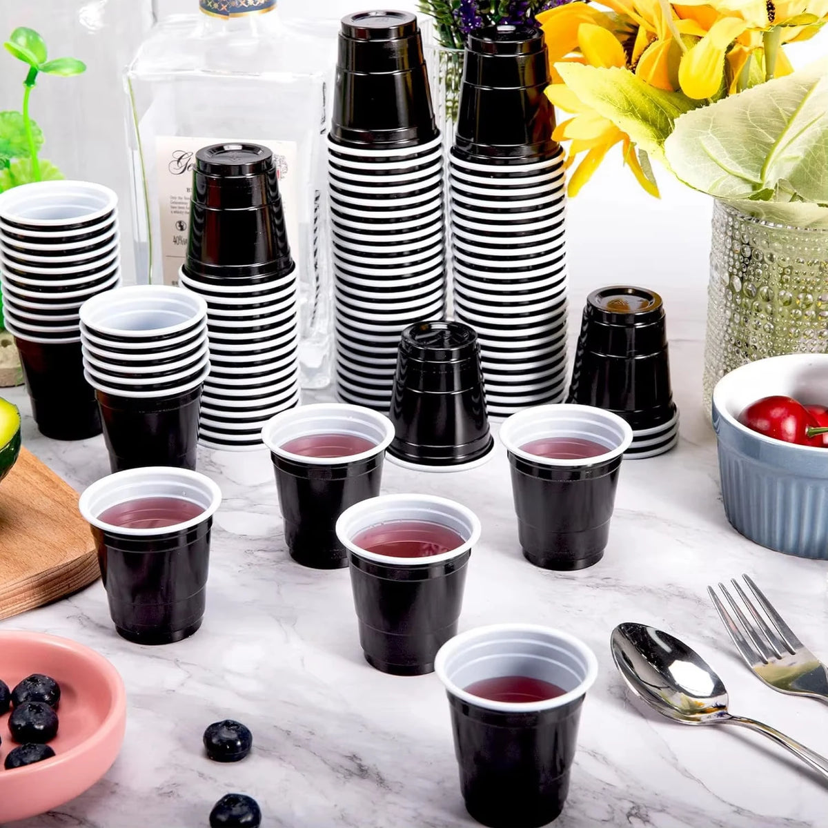 A collection of black and white striped mini plastic shot cups filled with red liquid on a white marble surface.