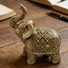 A detailed gold-colored resin elephant sculpture with intricate patterns, resting on a wooden surface.
