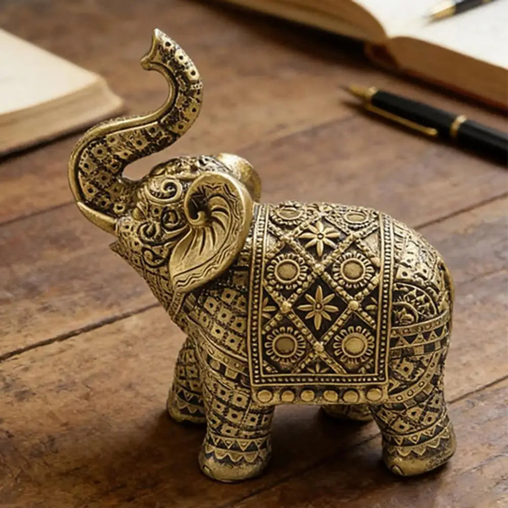 A detailed gold-colored resin elephant sculpture with intricate patterns, resting on a wooden surface.
