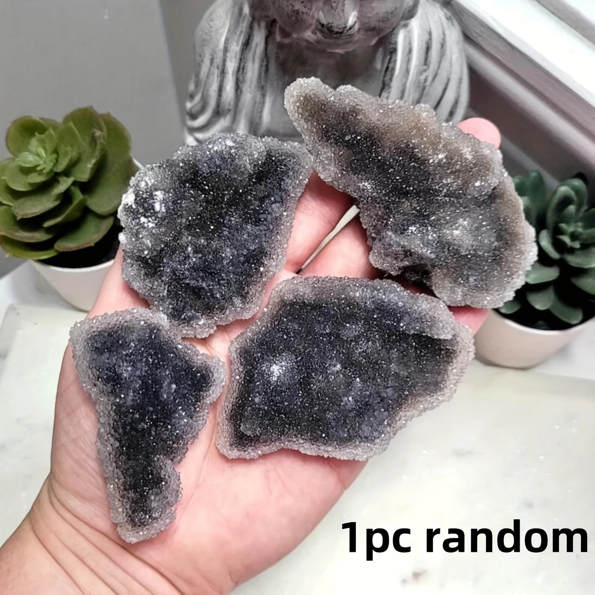 A hand holds a piece of dark gray natural zinc crystal cluster decor against a blurred background.