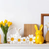 A set of three white and yellow wooden daisy flower ornaments displayed on a white shelf.