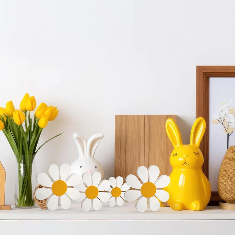 A set of three white and yellow wooden daisy flower ornaments displayed on a white shelf.