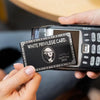A hand holds a white privilege card skin sticker decoration against a black electronic device.