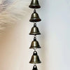 A vertical arrangement of five antique bronze metal wind chimes hanging against a white background.